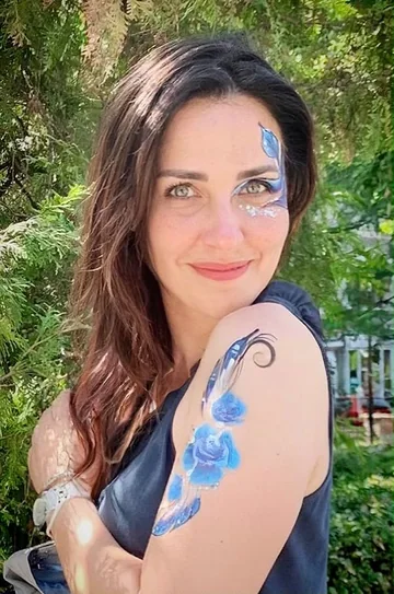 Mujer con flores azules pintadas en el rostro y el brazo, retrato cercano