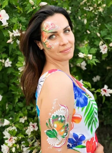 Mujer entre flores con mariposa multicolor pintada en el brazo y el rostro