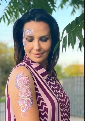 Mujer con flores rosas pintadas en el rostro y el brazo, retrato cercano