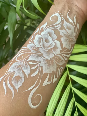 Flores blancas pintadas en el brazo sobre un fondo de hojas verdes