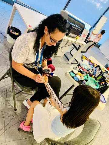 Tati pintando un diseño de cebra en el brazo de una niña