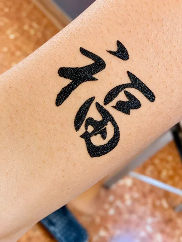 Tatuaje de glitter negro con un símbolo caligráfico