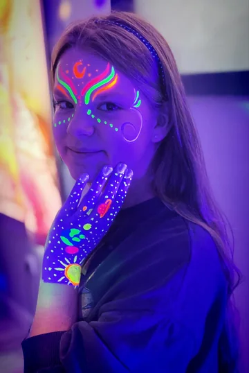 Maquillaje neón en el rostro y diseño espacial en la mano
