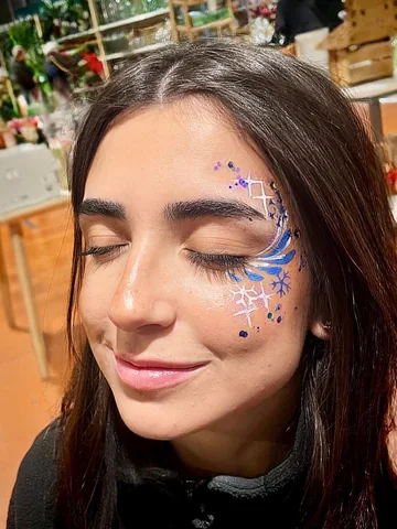 Joven con maquillaje azul y blanco con brillos alrededor del ojo