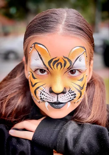 Niña con maquillaje de tigre dorado y colmillos blancos