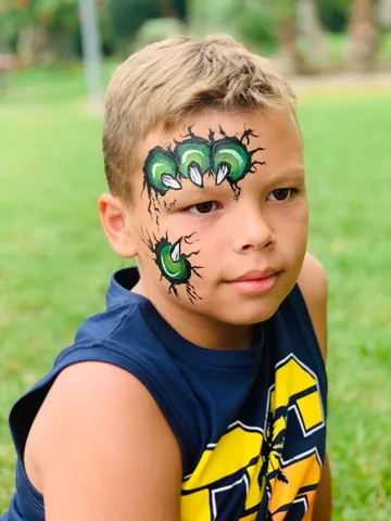 Niño con garras verdes pintadas en el rostro