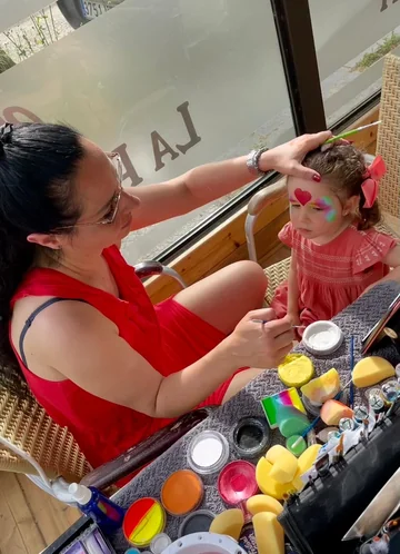 Tati pintando un corazón y colores de fantasía en el rostro de una niña
